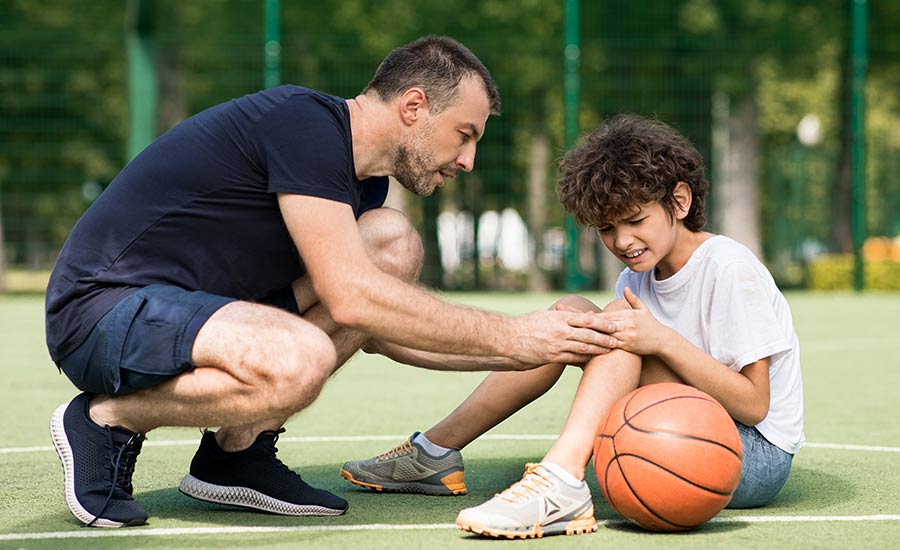 A coach helps a boy with a knee injury