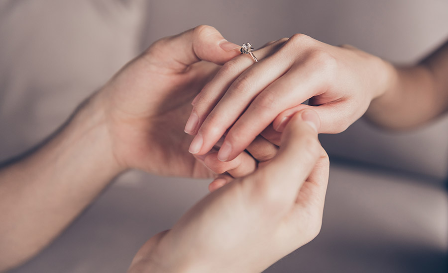 A man putting an engagement ring on his fiance's hand