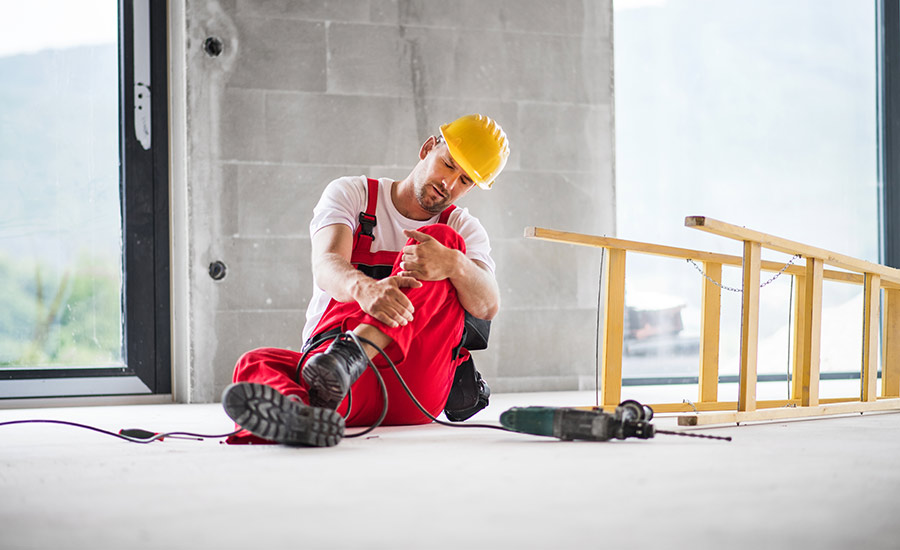 A construction worker with an injured knee next to a fallen ladder on a construction site​