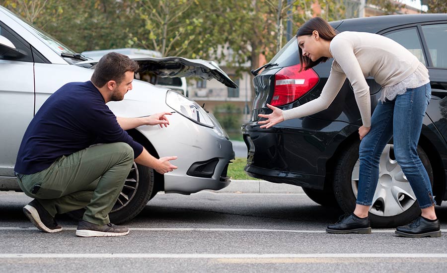 A woman and a man discussing damages on their vehicles after a rear-end collision​