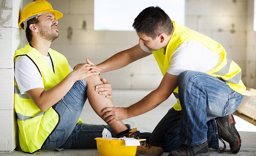 A construction worker helping a colleague who has suffered a leg injury​