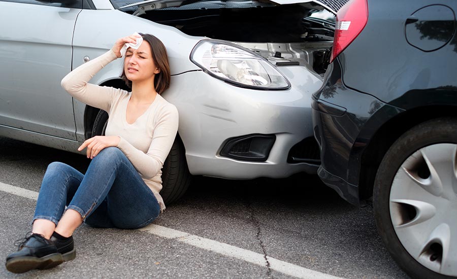 An injured woman sitting on the ground next to crashed cars​