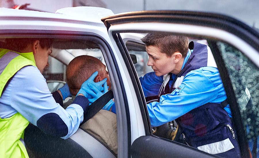 A rescue team tends to an injured person sitting in his car after a car accident​